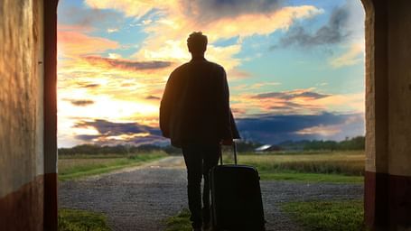 a person holding his luggage and walking towards an empty place with different hues in the sky above