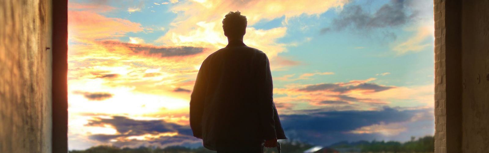 a person holding his luggage and walking towards an empty place with different hues in the sky above