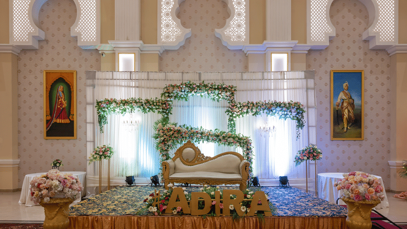 Decorated stage set up at Geeta Sarovar Portico, Panipat featuring a decorated chair in a stage which is decorated by flowers and light fabrics. On either sides there are paintings hung on the wall.