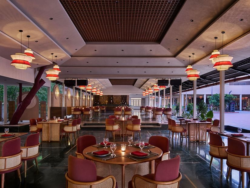 The interior of Zaika features numerous round tables with red chairs, illuminated by distinctive red and white hanging pendant lights.