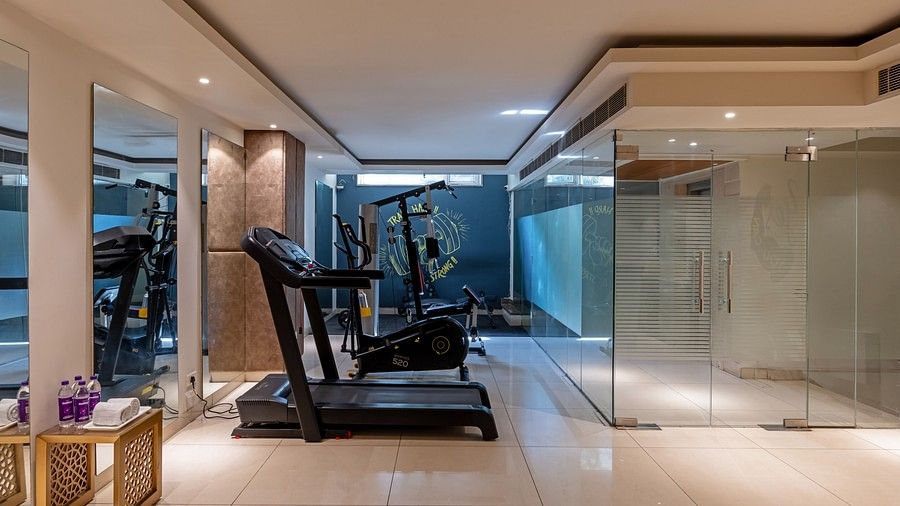 A fitness space outfitted with a treadmill, elliptical cross trainer,multi purpose gym mahcine and bench press machines, accompanied by a table stocked with water bottles and towels.