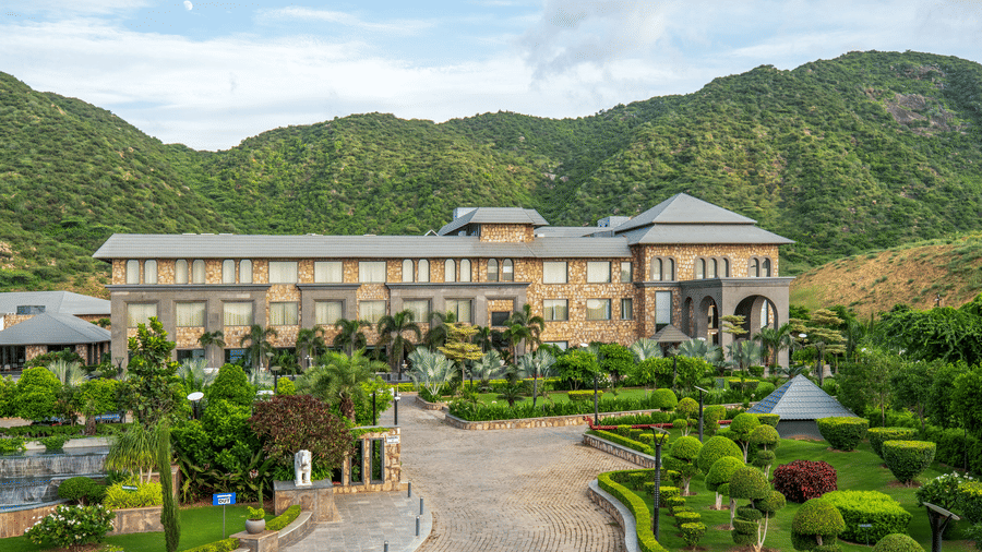 Facade of Pushkara Resort & Spa with a backdrop of mountains and surrounded by trees and shrubs.
