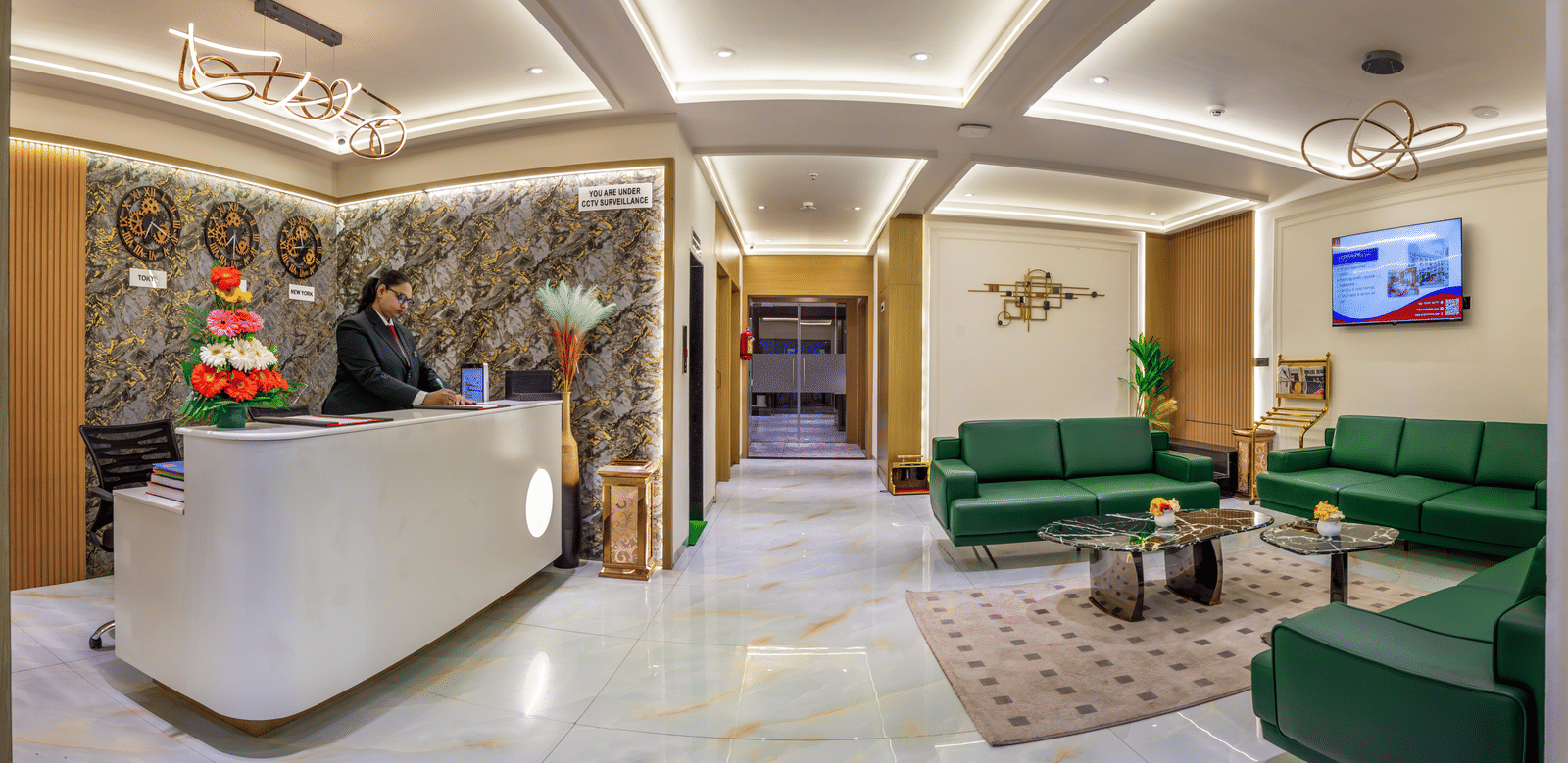 Stylish hotel reception and lounge area featuring a white front desk, green accent chairs, and contemporary decor at Lords Studio Inn, Jamnagar.