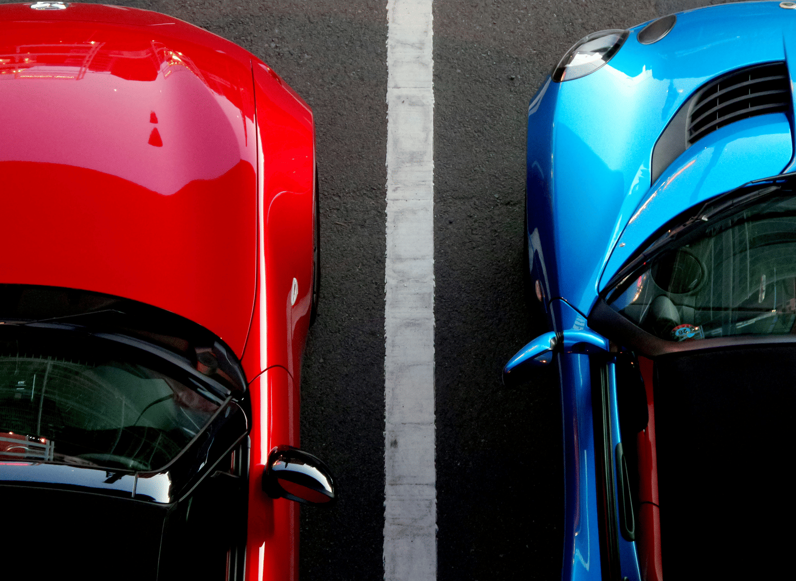 An overhead close-up of a bright red car parked next to a blue car in a car park.