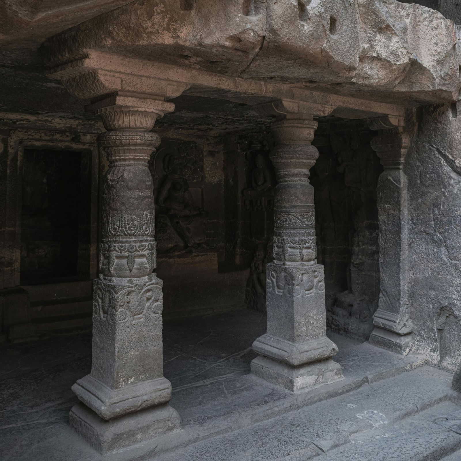 Interior of a rock-cut temple with carved stone pillars and small chambers, highlighting ancient architecture.