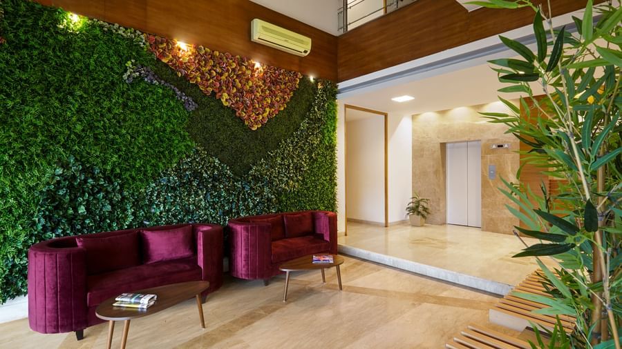 A modern lobby at Monday Hotels Mahape, Navi Mumbai, with a green wall, a red sofa, and wood accents.