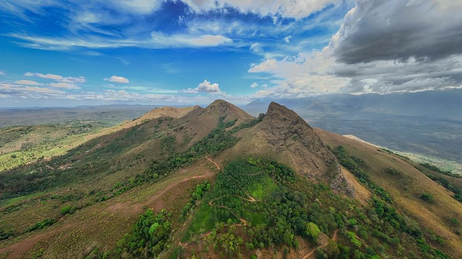 Panoramic aerial view of a rugged mountain ridge under a dramatic sky, with green valleys stretching into the horizon.