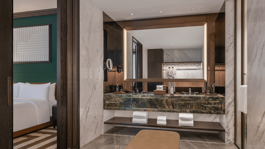 View of the Club Suite vanity area at The Residency Signature Madurai with a backlit mirror, marble countertop, and warm ambient lighting.