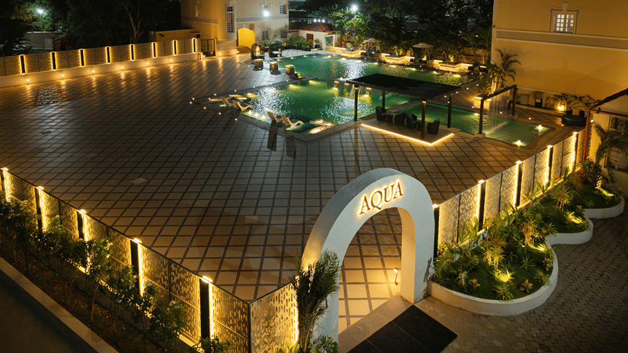 Night view of an outdoor pool complex with warm ambient lighting and an arched entrance marked Aqua at Jenneys Residency.