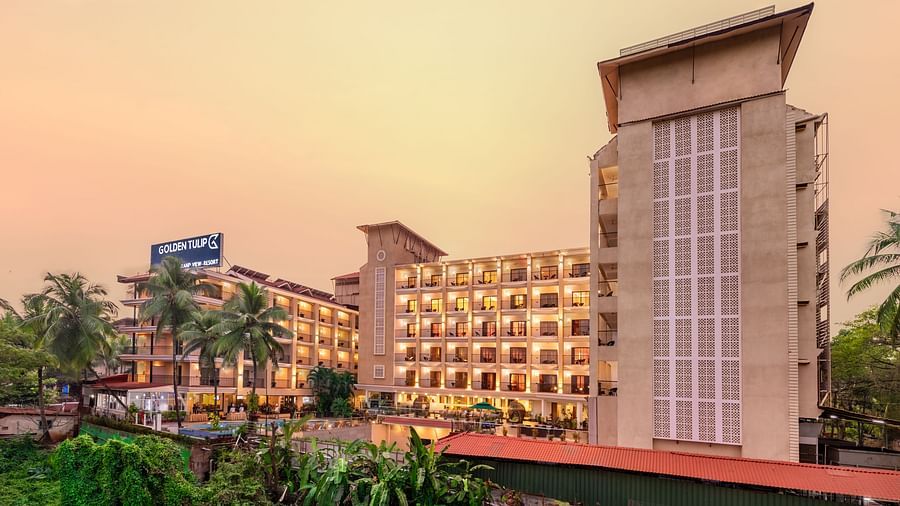 towering hotel buildings featuring balconies, a signage with hotel name, and surrounded by lush greenery, set against a golden hue filed sky - Golden Tulip, Candolim, Goa