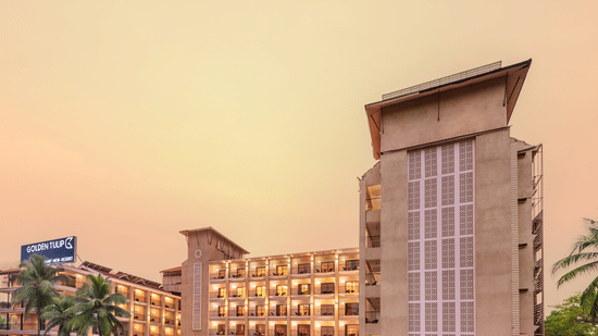 towering hotel buildings featuring balconies, a signage with hotel name, and surrounded by lush greenery, set against a golden hue filed sky - Golden Tulip, Candolim, Goa
