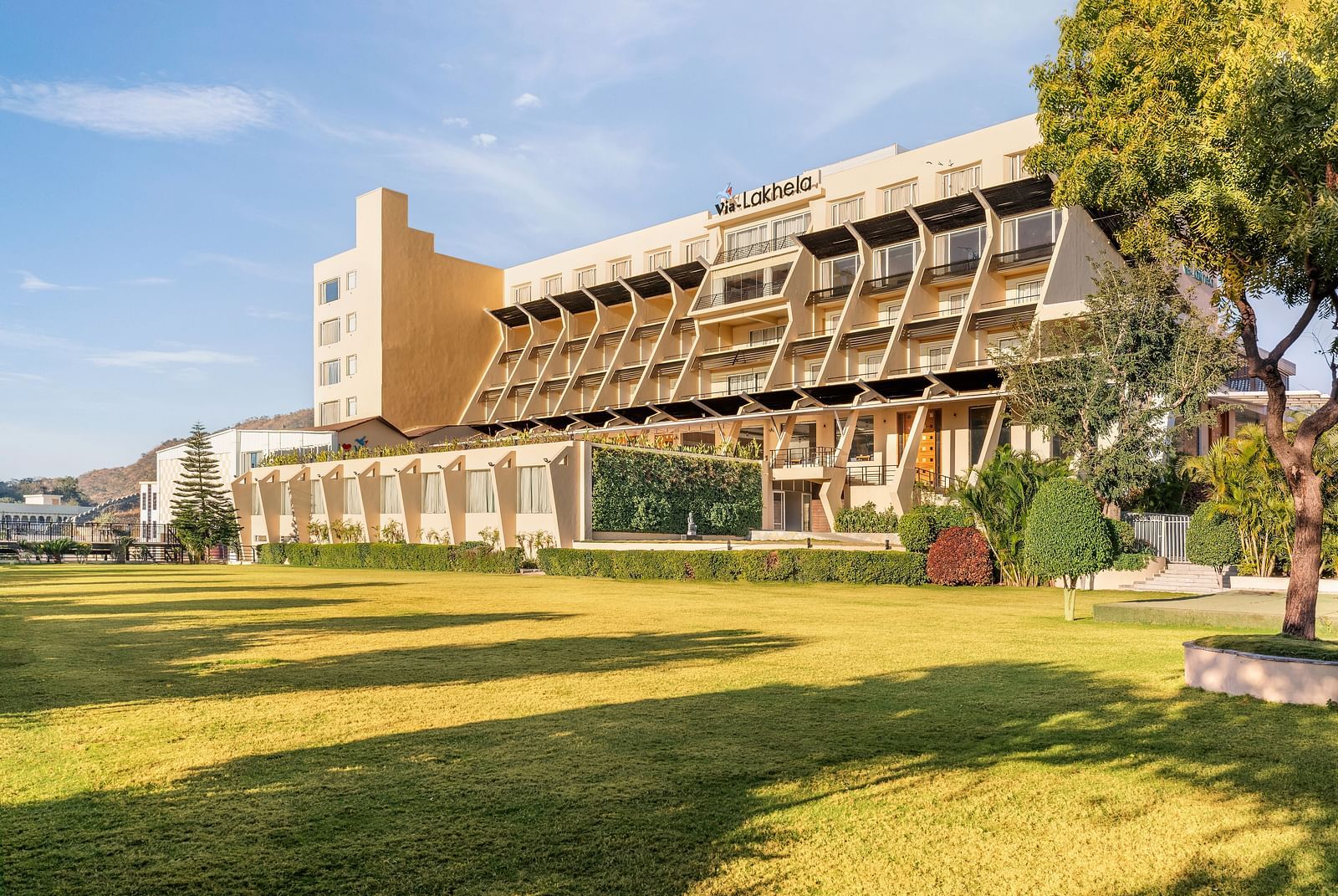 A large building with a tower with trees and a sunny outdoor scene - Via Lakhela Resort & Spa