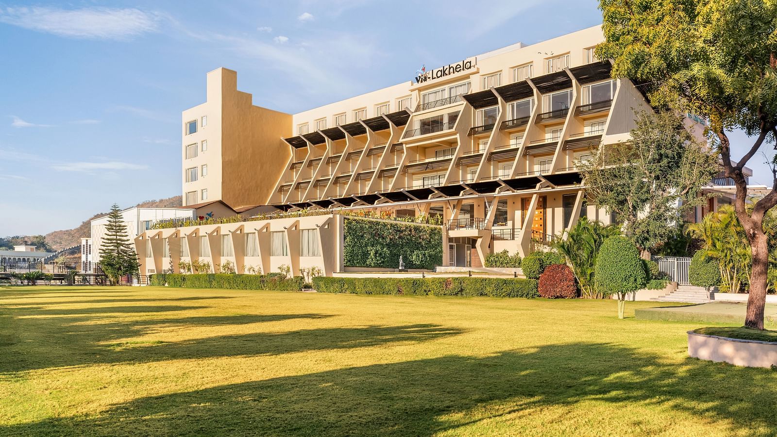 A large building with a tower with trees and a sunny outdoor scene - Via Lakhela Resort & Spa
