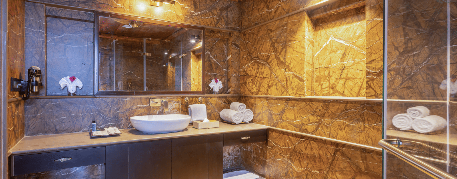 A contemporary bathroom at Aamaghati Wildlife Resort with elegant stone interiors, warm lighting, and modern amenities.