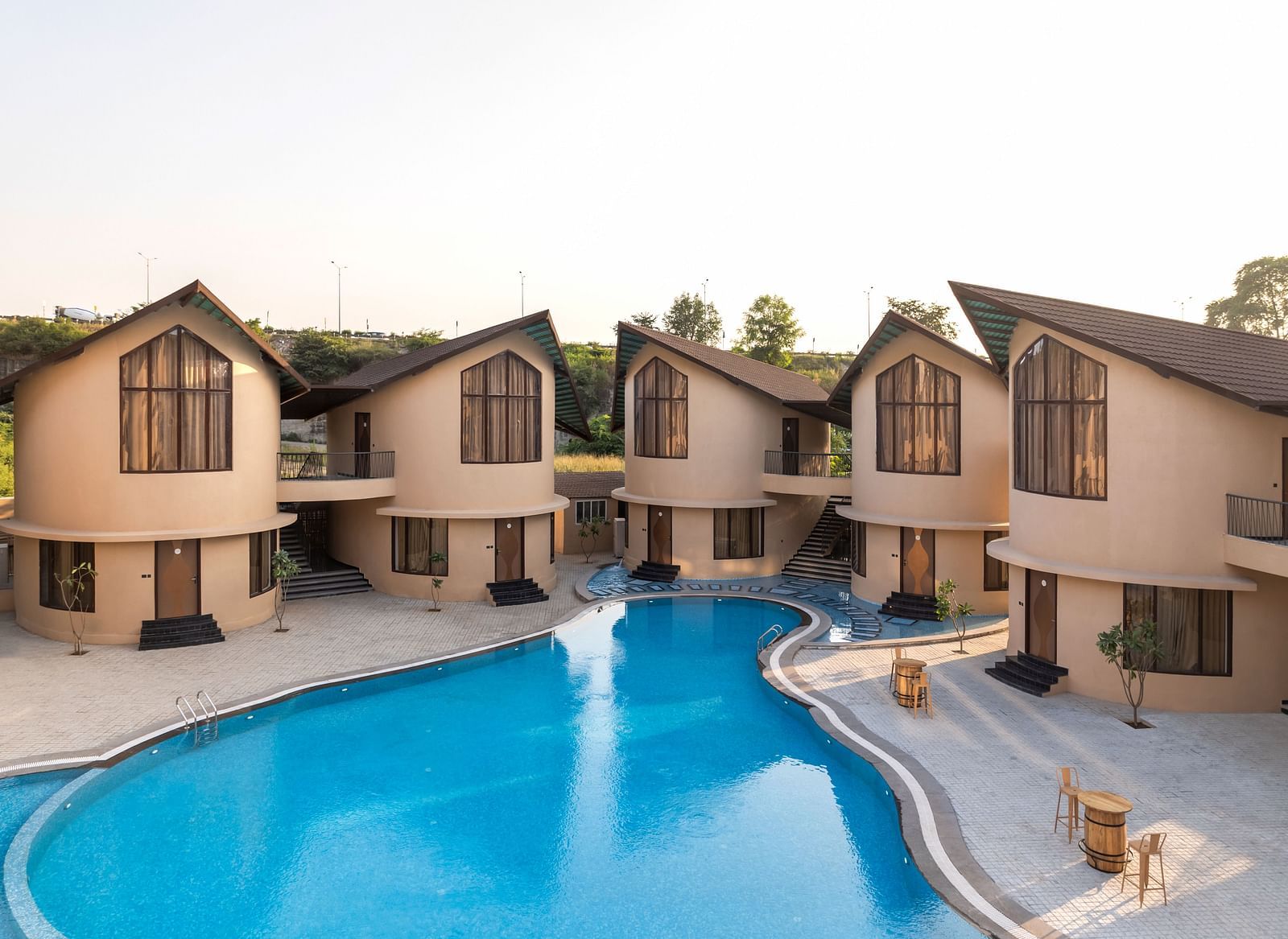 The Qualia Resort Club & Brewery, Udaipur showcasing multiple villas surrounding a curved swimming pool.