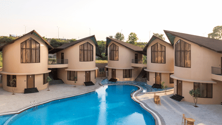 The Qualia Resort Club & Brewery, Udaipur showcasing multiple villas surrounding a curved swimming pool.