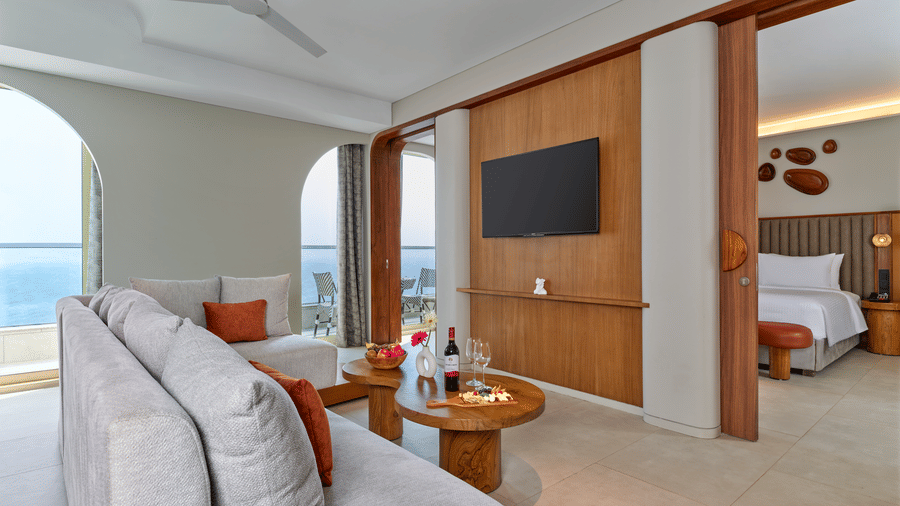 The Intimate Escape Suite living room at Swosti Premium Beach Resorts, Puri, with sofas, a television, and a door revealing a bedroom.