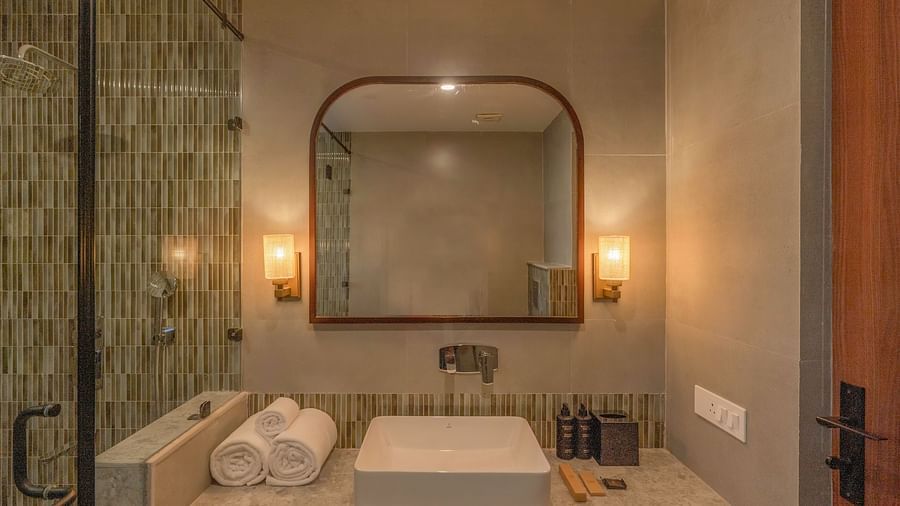 A bathroom with a large sink, essentials on one side, rolled towels on the other, and a wall-mounted mirror above it at The Chamomile Estate.