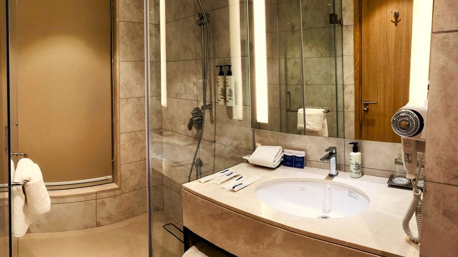 A luxurious bathroom in the Executive Room at Golden Sarovar Portico, Amritsar, featuring a marble counter with a large inset wash basin, a well-lit mirror, and modern chrome fittings.