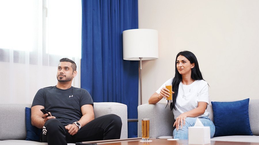Two people sitting on a couch in a seating area at La Maison, Doha, with cleaning supplies on a table.
