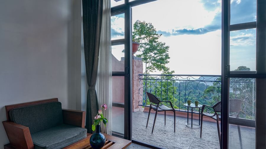 Seating area adjacent to glass doors opening to a balcony with outdoor furniture and a picturesque view of the surrounding landscape. | Mango Hill, Yercaud