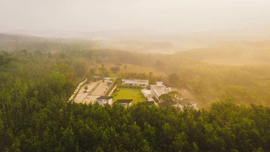 A view of the Bindiga Peak Resort surrounded by a dense green forest under a misty sky.