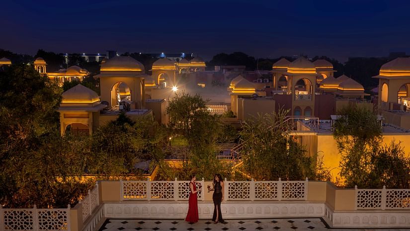 A couple stands on a spacious terrace overlooking a luxury resort illuminated by warm golden lights, surrounded by a serene ambience