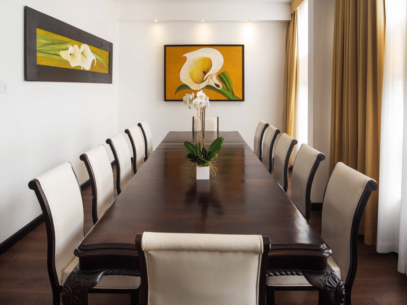 A  boardroom featuring a long, dark wood boardroom table surrounded by approximately ten high-back upholstered chairs in S Hotels Kingston.