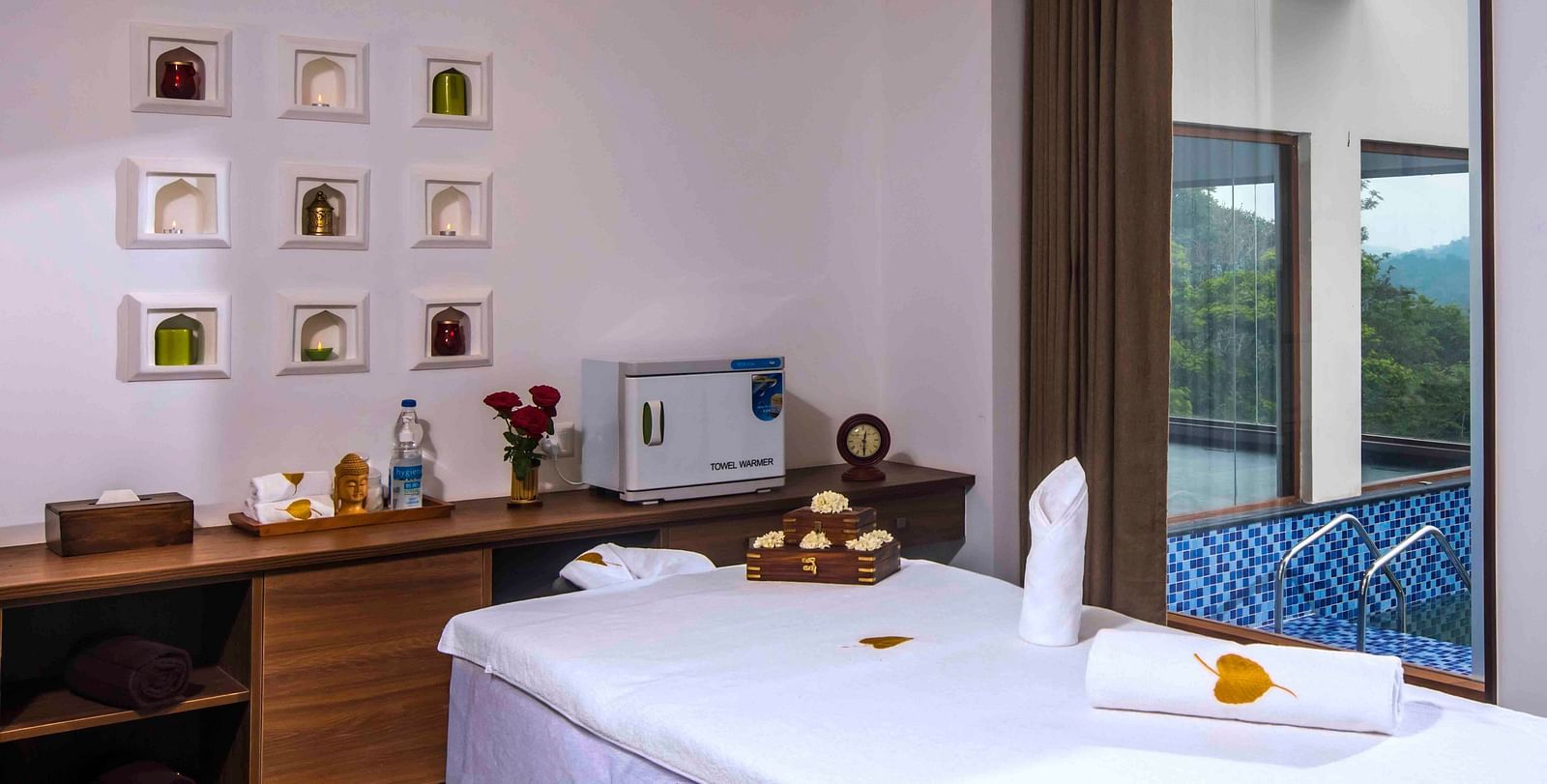 Image of the bed at the spa along with some wall decor and a table Drone shot of the hotel | Great Trails Wayanad by  GRT hotels.