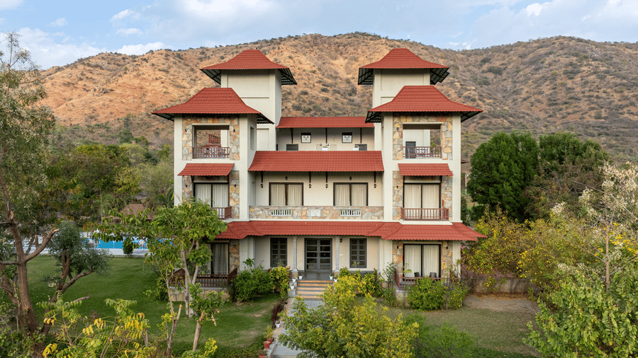 Front view of The Hunting Lodge, Udaipur's facade with lush green lawns and beautiful plants in the foreground.