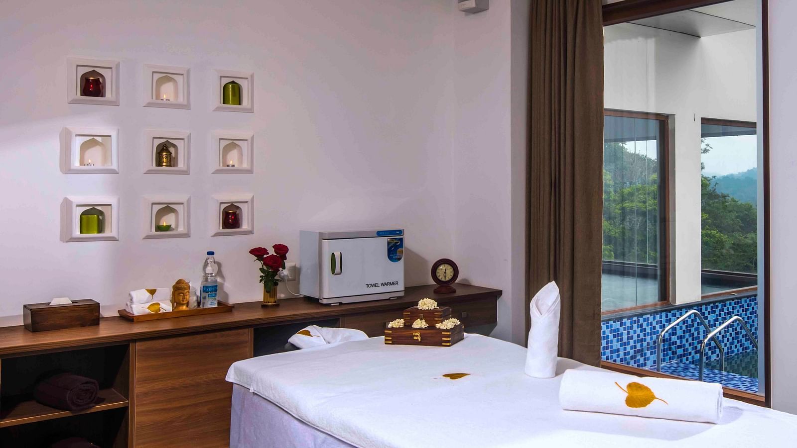 Image of the bed at the spa along with some wall decor and a table Drone shot of the hotel | Great Trails Wayanad by  GRT hotels.