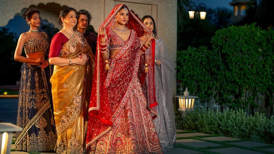 Four women in traditional indian sarees pose together at dusk, with soft lighting and a garden in the background.