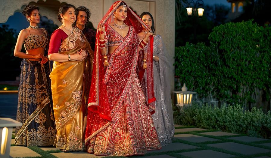 Four women in traditional indian sarees pose together at dusk, with soft lighting and a garden in the background.