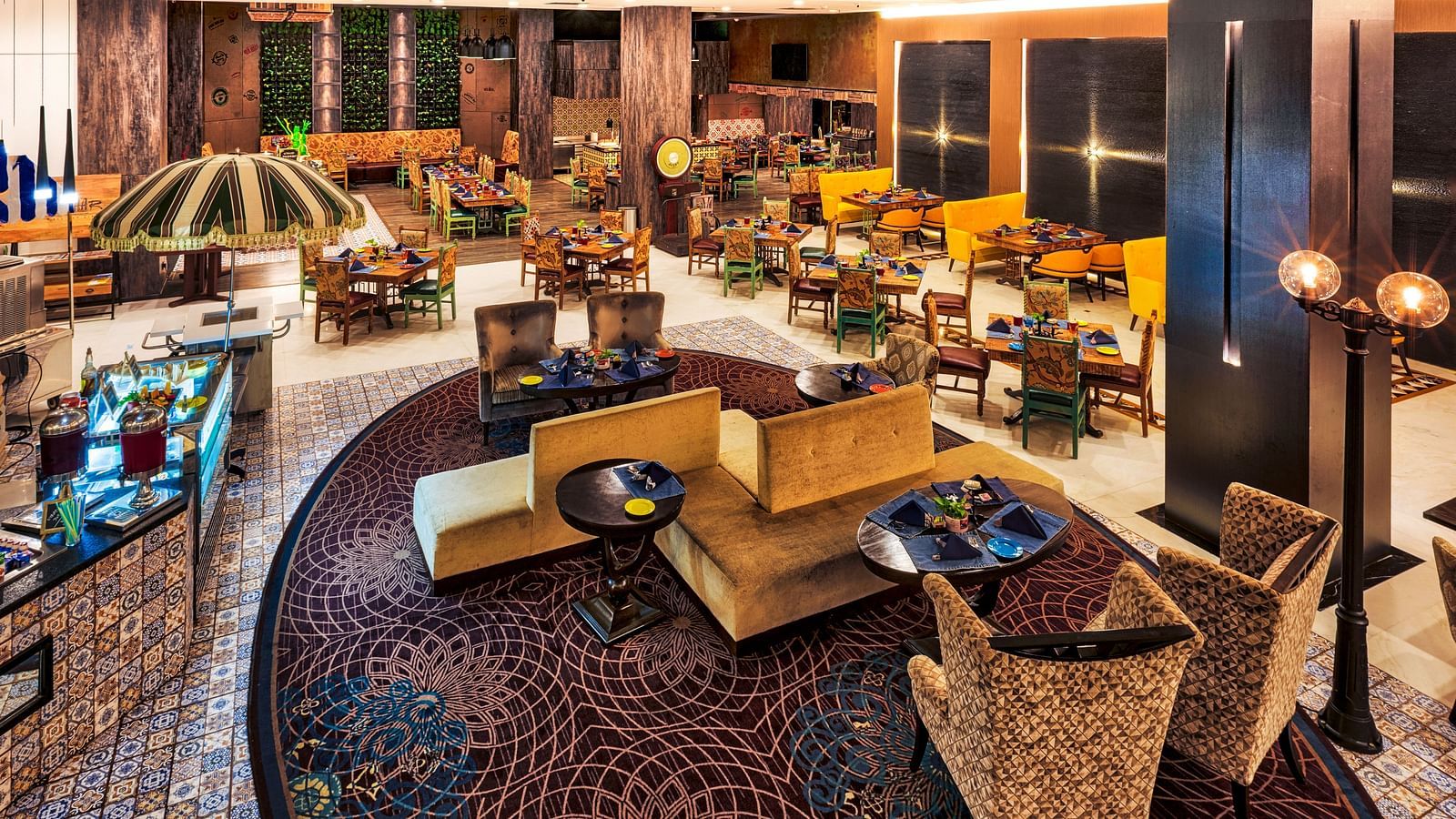 A stylish restaurant features varied seating arrangements, including cushioned chairs around tables and sofa-style seating, under warm lighting - Grand Chennai by GRT Hotels