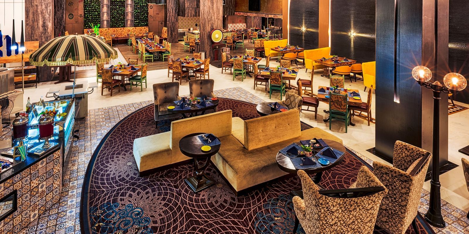A stylish restaurant features varied seating arrangements, including cushioned chairs around tables and sofa-style seating, under warm lighting - Grand Chennai by GRT Hotels