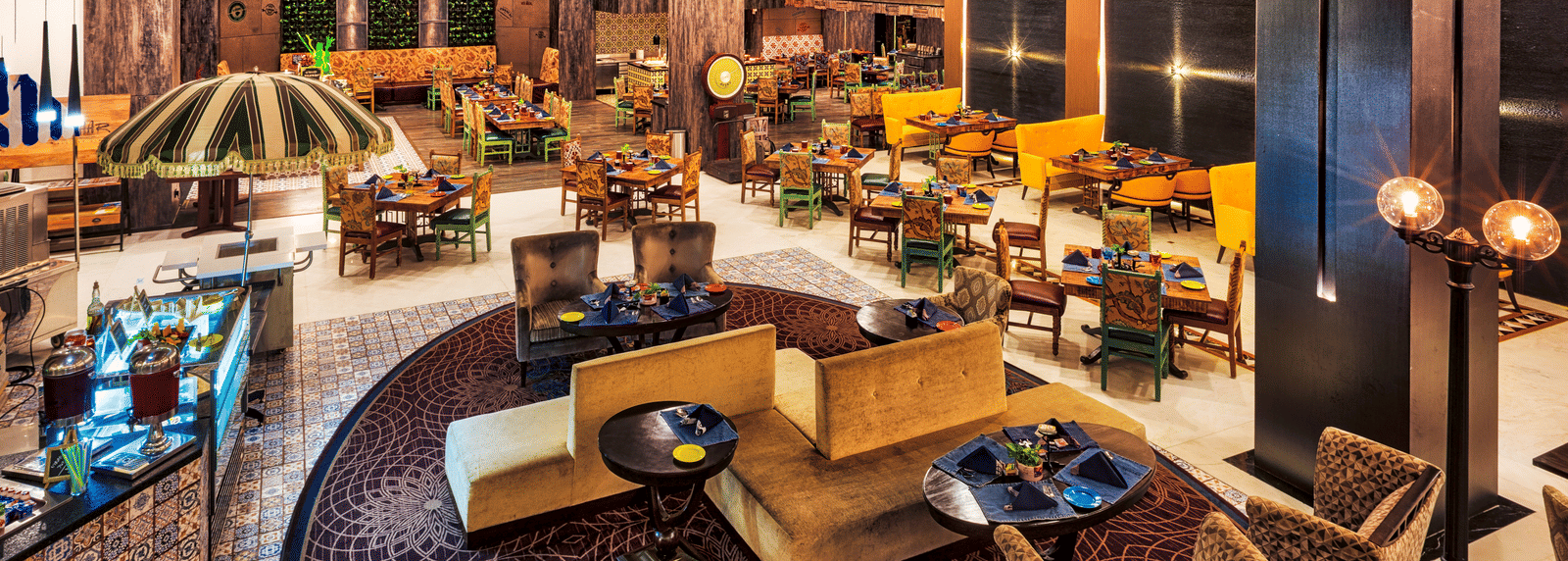 A stylish restaurant features varied seating arrangements, including cushioned chairs around tables and sofa-style seating, under warm lighting - Grand Chennai by GRT Hotels