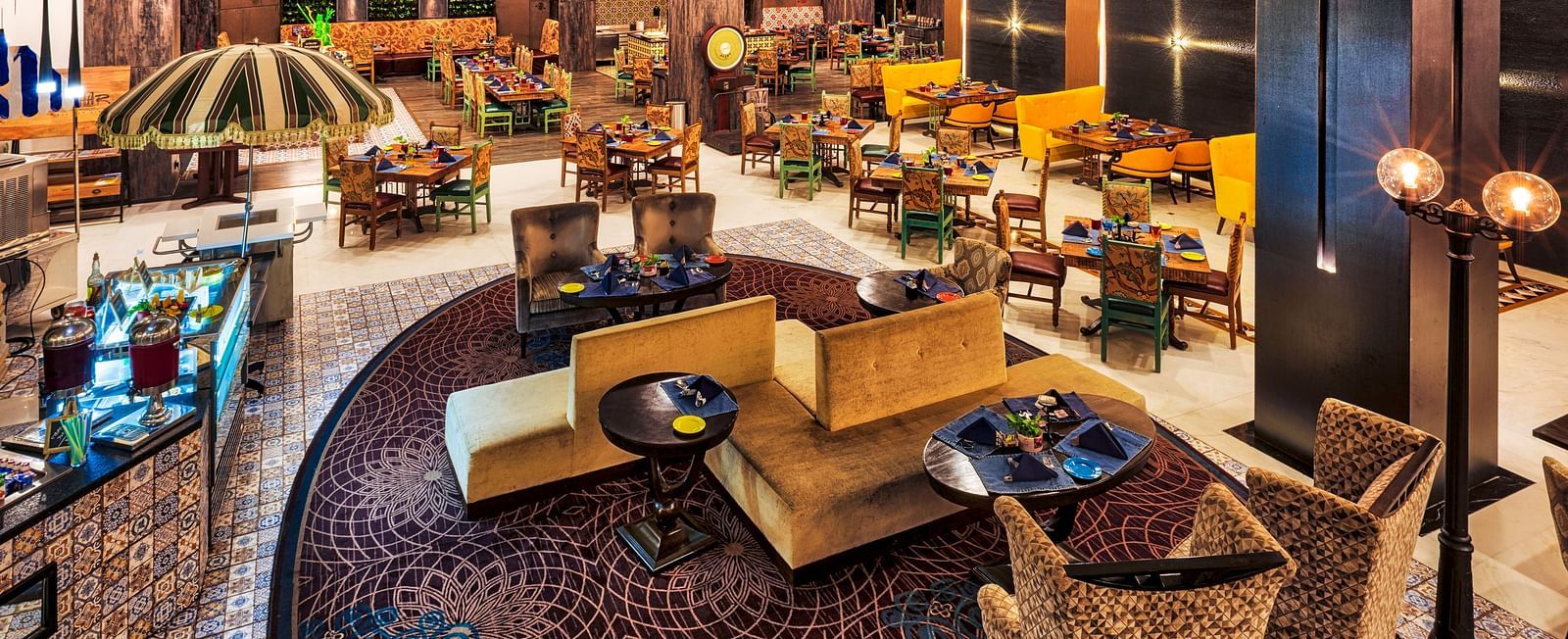 A stylish restaurant features varied seating arrangements, including cushioned chairs around tables and sofa-style seating, under warm lighting - Grand Chennai by GRT Hotels