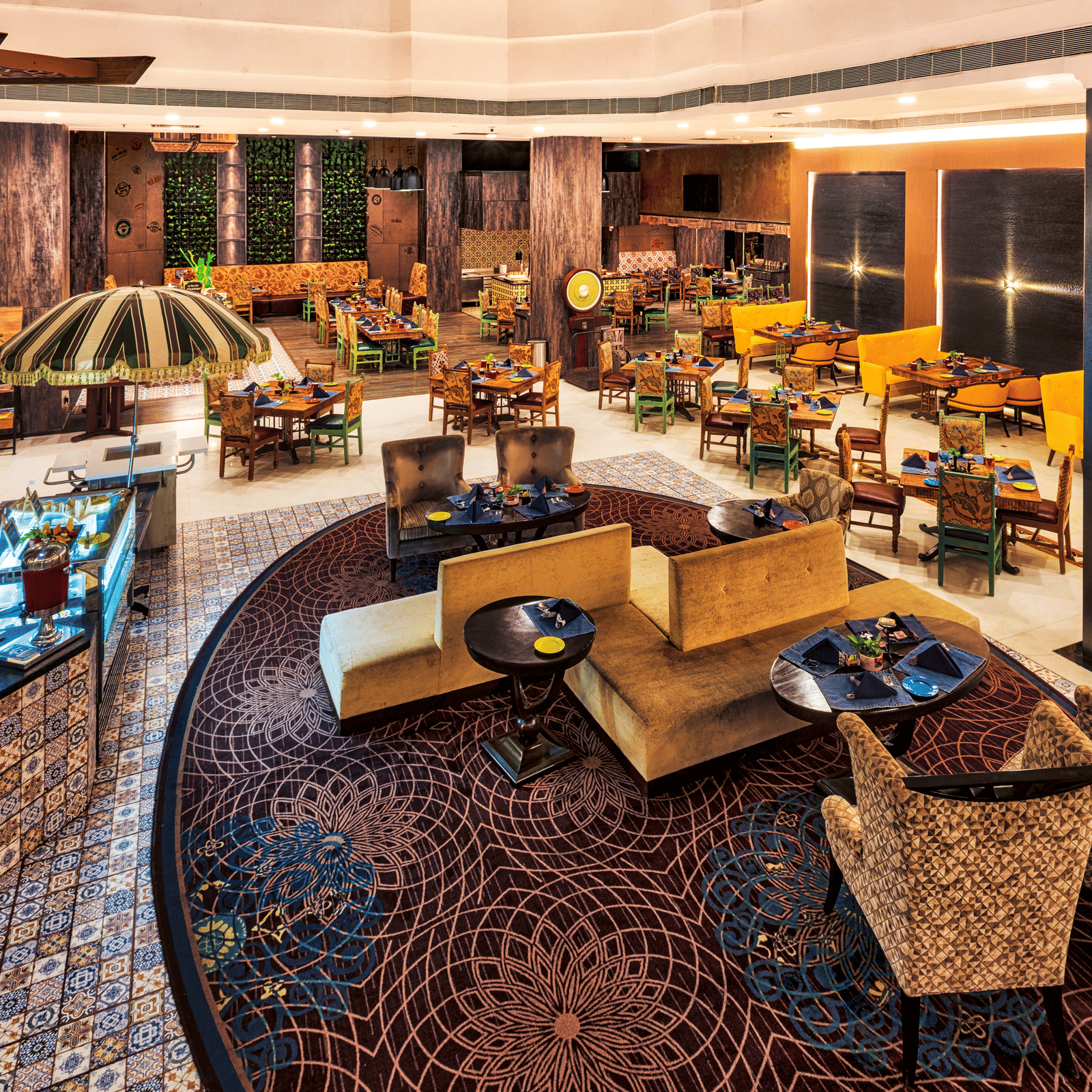 A stylish restaurant features varied seating arrangements, including cushioned chairs around tables and sofa-style seating, under warm lighting - Grand Chennai by GRT Hotels