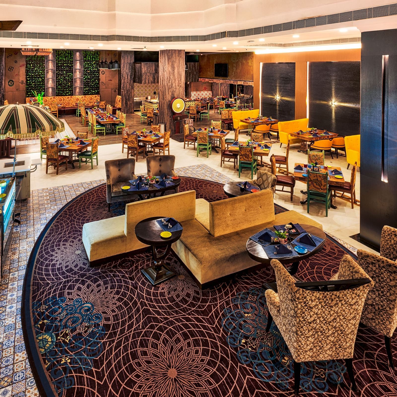 A stylish restaurant features varied seating arrangements, including cushioned chairs around tables and sofa-style seating, under warm lighting - Grand Chennai by GRT Hotels