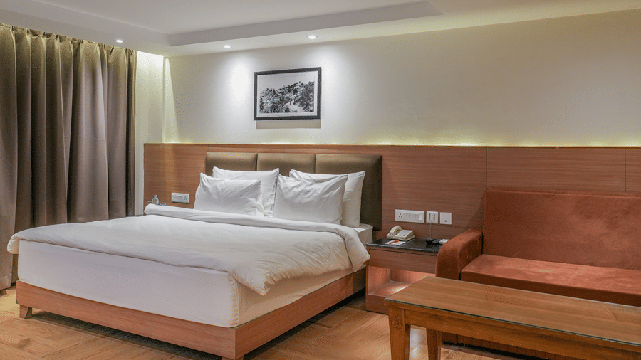 A room featuring a queen size bed, a wooden sofa with a coffee table, wood paneling, and warm lighting at Ramada by Wyndham Mussoorie Mall Road.