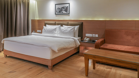 A room featuring a queen size bed, a wooden sofa with a coffee table, wood paneling, and warm lighting at Ramada by Wyndham Mussoorie Mall Road.