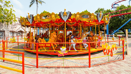 Carousel with painted horses under a red and gold canopy and a Family Ride sign, enclosed by red and yellow railings on paving at MGM Dizzee World, Chennai.