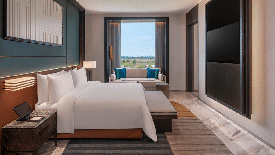 View of the Premium Suite bedroom at The Residency Signature Madurai with a king bed, wall-mounted TV, large window, and warm ambient lighting.