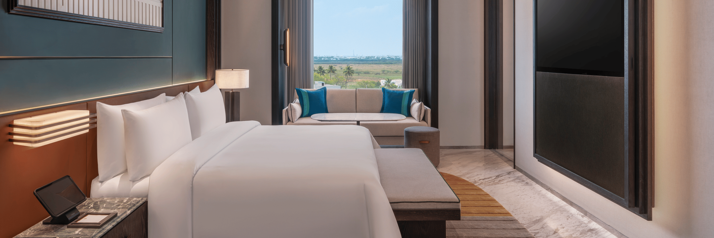 Contemporary Premium Suite bedroom at The Residency Signature Madurai with a neatly made bed, a window looking outside, and a wall-mounted television panel.
