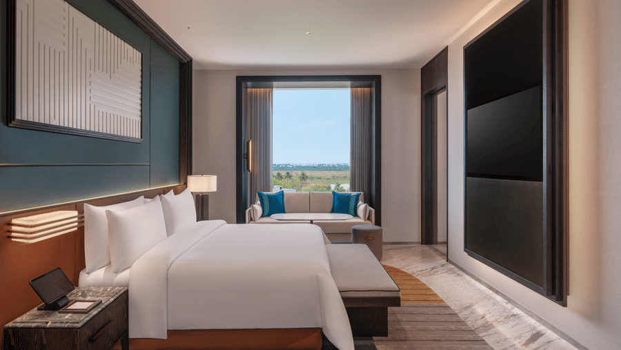 Contemporary Premium Suite bedroom at The Residency Signature Madurai with a neatly made bed, a window looking outside, and a wall-mounted television panel.