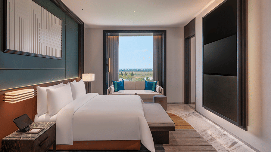 View of the Premium Suite bedroom at The Residency Signature Madurai with a king bed, wall-mounted TV, large window, and warm ambient lighting.