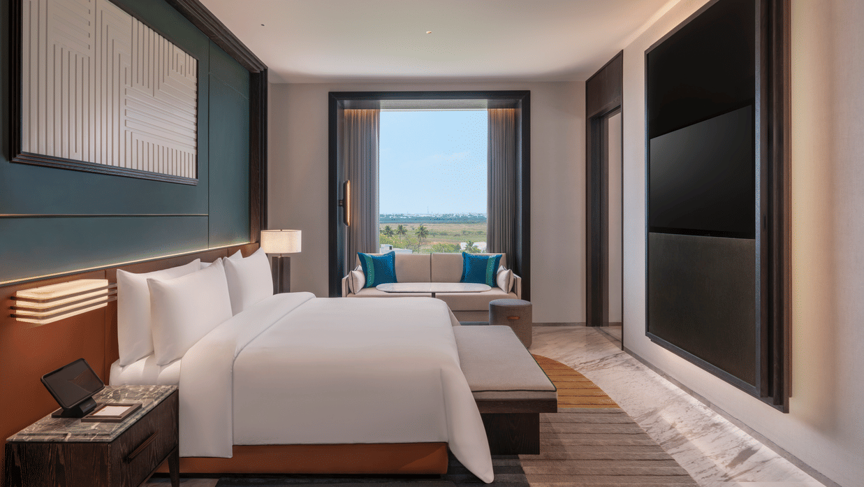 View of the Premium Suite bedroom at The Residency Signature Madurai with a king bed, wall-mounted TV, large window, and warm ambient lighting.