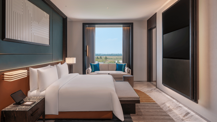 View of the Premium Suite bedroom at The Residency Signature Madurai with a king bed, wall-mounted TV, large window, and warm ambient lighting.