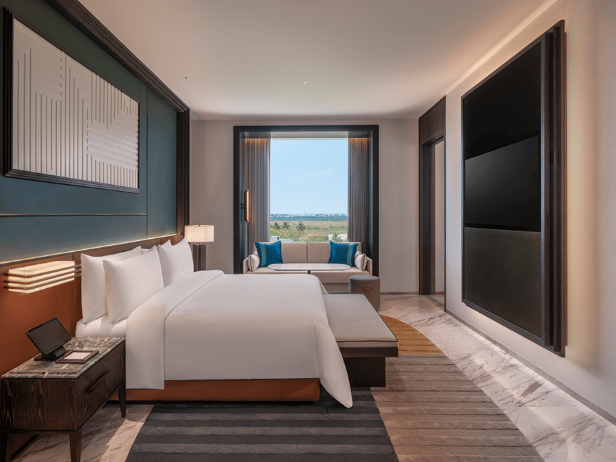 View of the Premium Suite bedroom at The Residency Signature Madurai with a king bed, wall-mounted TV, large window, and warm ambient lighting.