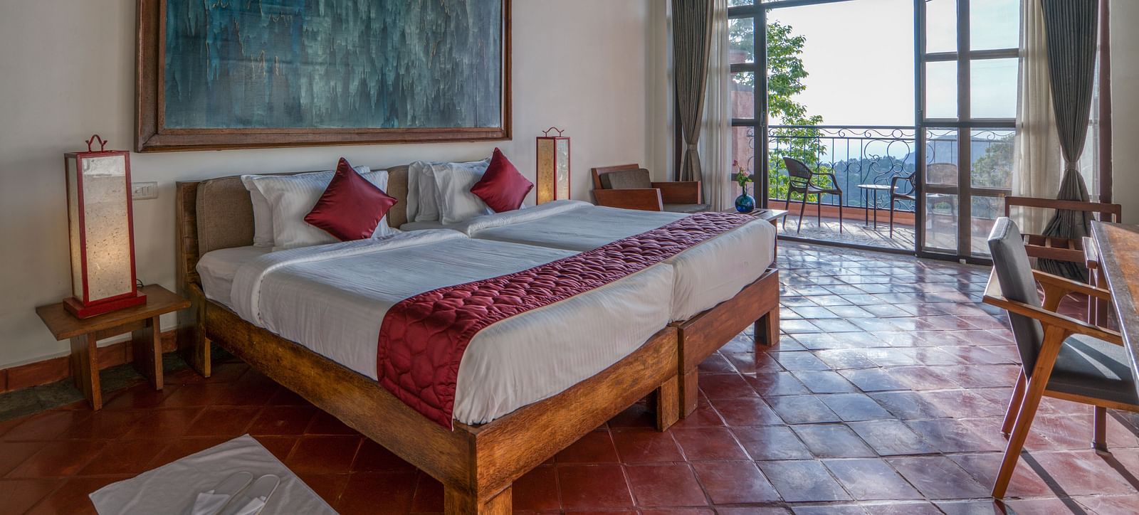 Bedroom featuring a king-size bed with red accents, large artwork, wooden furniture, and a balcony with a scenic view. | Mango Hill, Yercaud